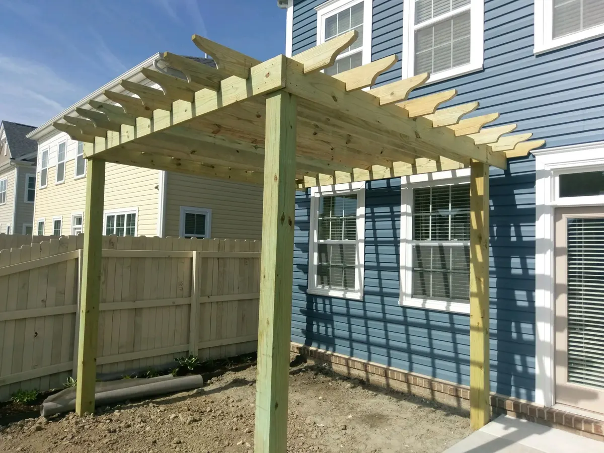 New pressure-treated custom pergola built against a blue Virginia Beach home beside a wood privacy fence